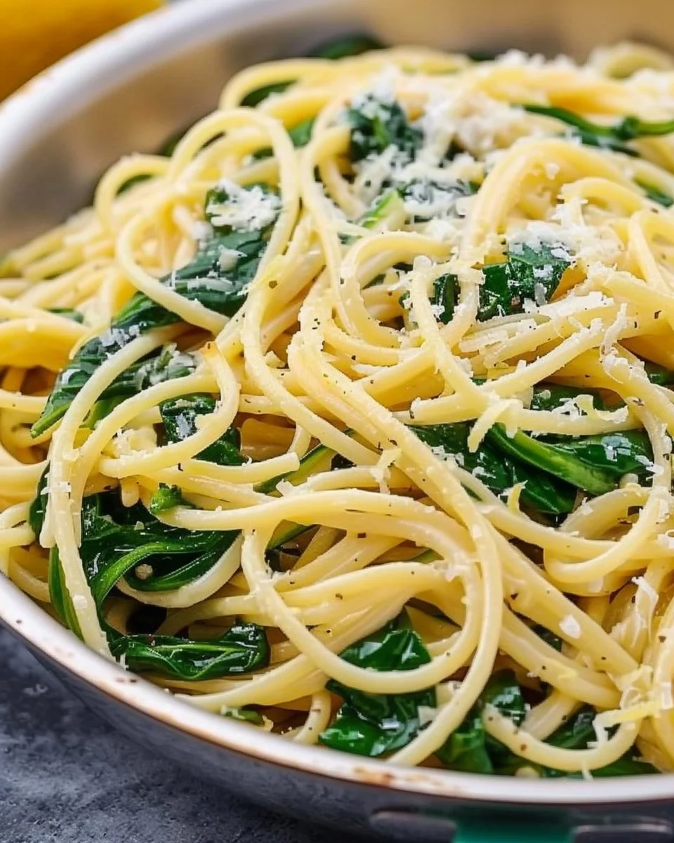 A bowl of lemon-spinach pasta garnished with fresh lemon slices and spinach leaves.